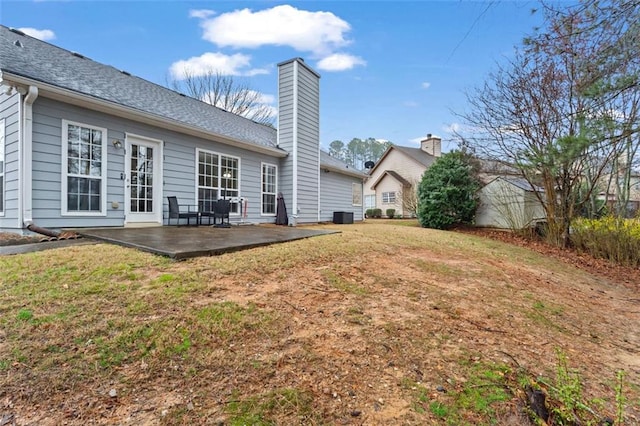 back of house featuring a yard, a chimney, a patio, and a shingled roof