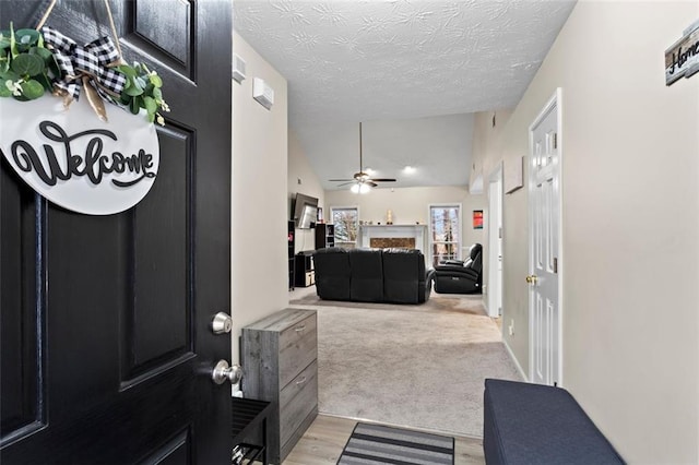 foyer featuring light wood-type flooring, light carpet, a ceiling fan, a textured ceiling, and vaulted ceiling