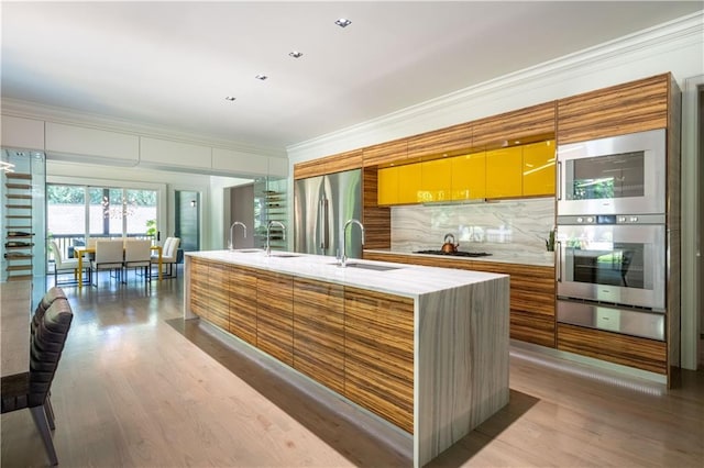 kitchen featuring a sink, ornamental molding, appliances with stainless steel finishes, a warming drawer, and an island with sink