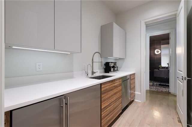 kitchen featuring light countertops, stainless steel dishwasher, modern cabinets, and a sink