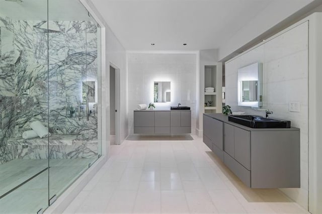 full bathroom with a marble finish shower, tile walls, two vanities, and a sink