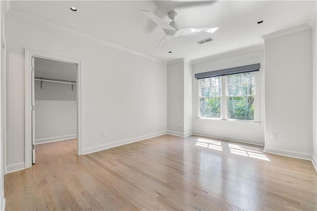 unfurnished bedroom featuring a walk in closet, visible vents, ornamental molding, light wood-type flooring, and baseboards