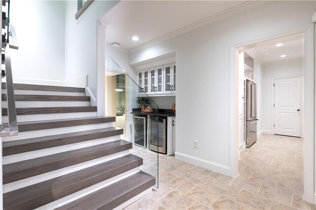 stairs with ornamental molding, beverage cooler, baseboards, and a bar