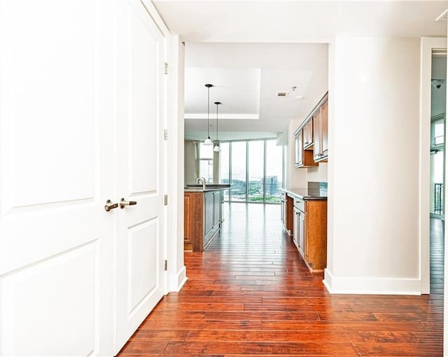 corridor with dark wood finished floors, a tray ceiling, and baseboards