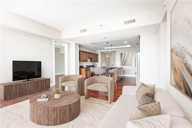 living area featuring light wood finished floors, a tray ceiling, and baseboards