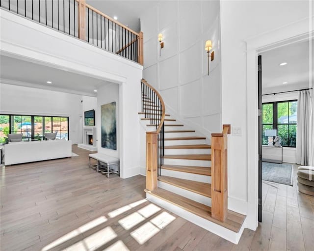 stairway featuring wood-type flooring, recessed lighting, a towering ceiling, and a lit fireplace