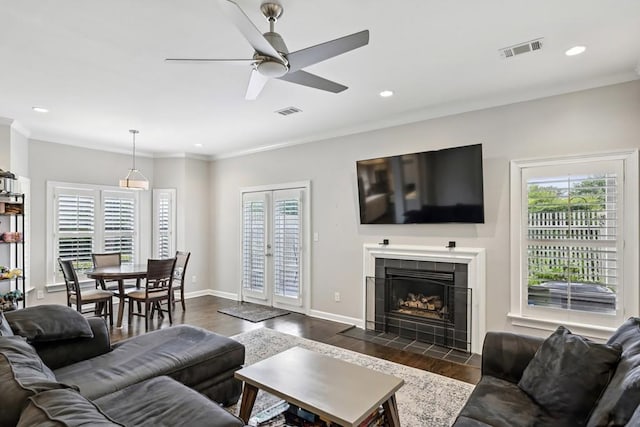 living room with healthy amount of natural light, dark wood-style flooring, ceiling fan, a fireplace, and crown molding