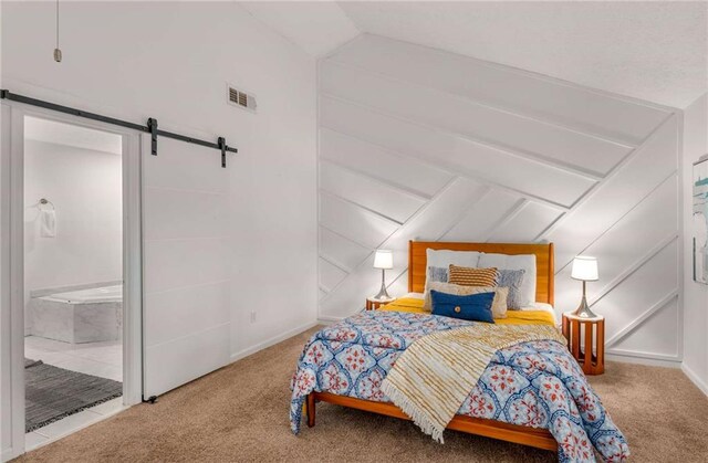 bedroom featuring carpet, ensuite bath, a barn door, and vaulted ceiling