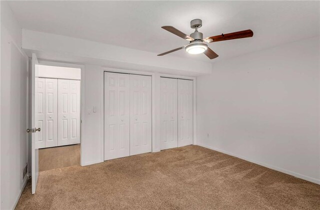 unfurnished bedroom featuring carpet, ceiling fan, and multiple closets