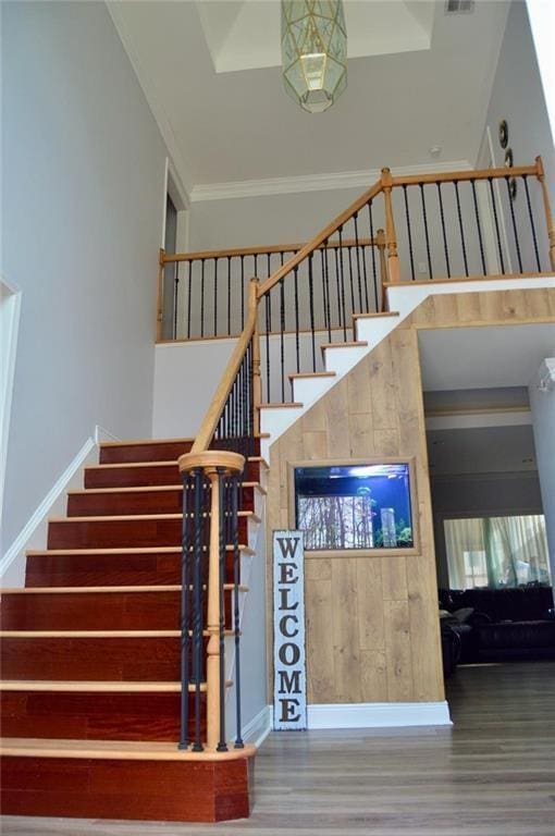 stairway featuring ornamental molding, a towering ceiling, and hardwood / wood-style floors