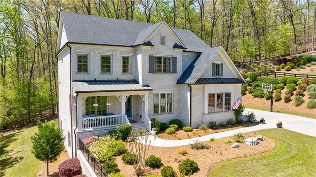 view of front facade with a standing seam roof, brick siding, metal roof, a porch, and driveway