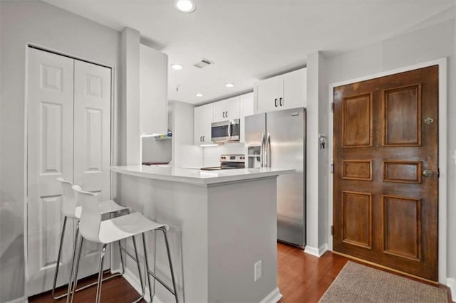 kitchen featuring light countertops, white cabinets, a peninsula, dark wood-style floors, and stainless steel appliances