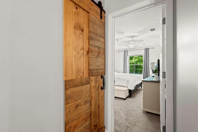 hall featuring a textured ceiling, visible vents, a barn door, and carpet