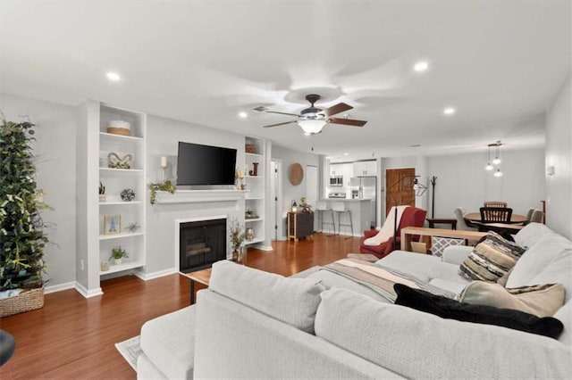 living room featuring ceiling fan, a fireplace, recessed lighting, baseboards, and wood finished floors
