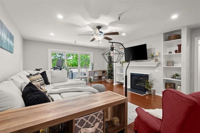 living room featuring a fireplace, built in features, a ceiling fan, recessed lighting, and wood finished floors