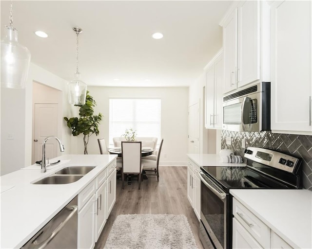 kitchen with a sink, white cabinets, light countertops, appliances with stainless steel finishes, and pendant lighting