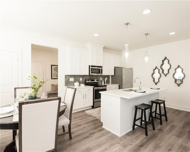 kitchen featuring a center island with sink, appliances with stainless steel finishes, hanging light fixtures, light countertops, and a sink