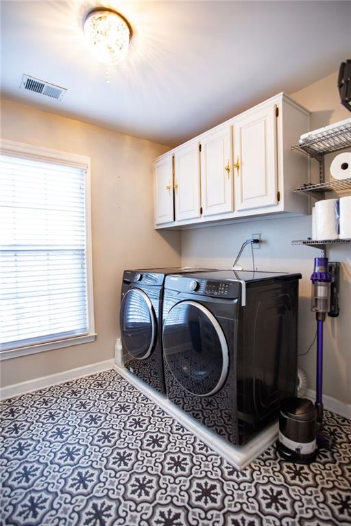 clothes washing area with cabinets, a wealth of natural light, and washing machine and clothes dryer