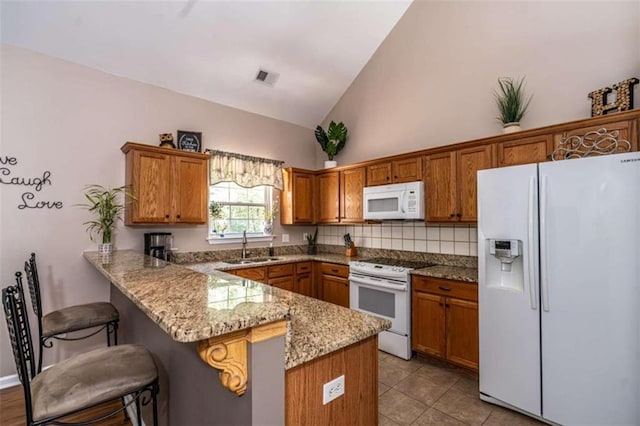 kitchen with a breakfast bar area, lofted ceiling, kitchen peninsula, white appliances, and light stone countertops