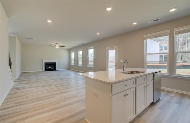 kitchen with white cabinetry, dishwasher, sink, a center island with sink, and light hardwood / wood-style flooring