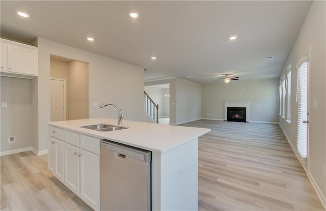 kitchen with sink, white cabinetry, light wood-type flooring, stainless steel dishwasher, and an island with sink