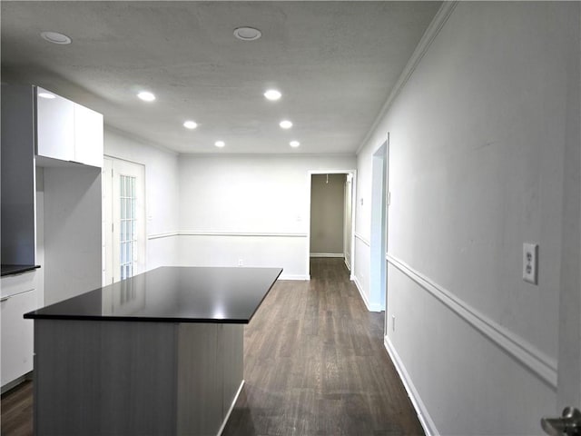 kitchen with dark wood-type flooring, ornamental molding, a kitchen island, and white cabinets