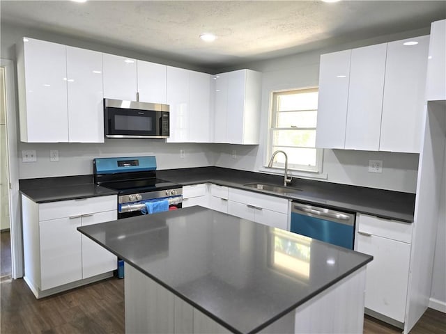 kitchen with a kitchen island, appliances with stainless steel finishes, white cabinetry, sink, and dark hardwood / wood-style flooring