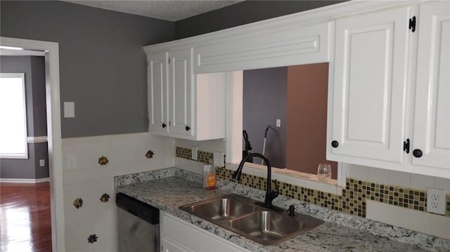 kitchen featuring light stone countertops, white cabinets, stainless steel dishwasher, and sink