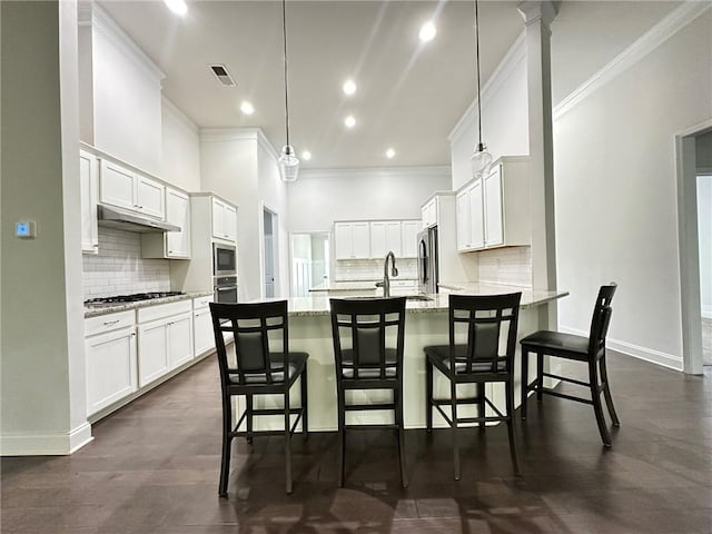 kitchen featuring a kitchen bar, light stone counters, hanging light fixtures, ornamental molding, and white cabinetry