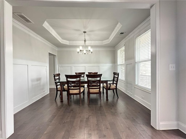 dining area with dark wood-type flooring, a chandelier, crown molding, and a raised ceiling