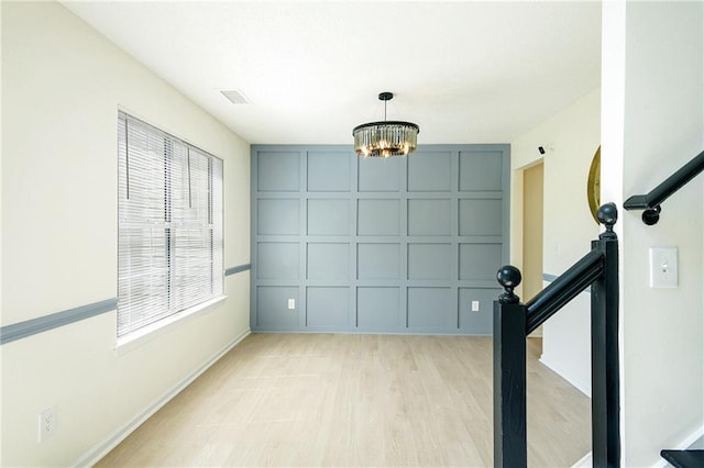 interior space featuring a chandelier, a decorative wall, visible vents, and light wood-style flooring