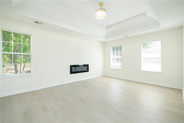 unfurnished living room with heating unit, a tray ceiling, light wood finished floors, and plenty of natural light