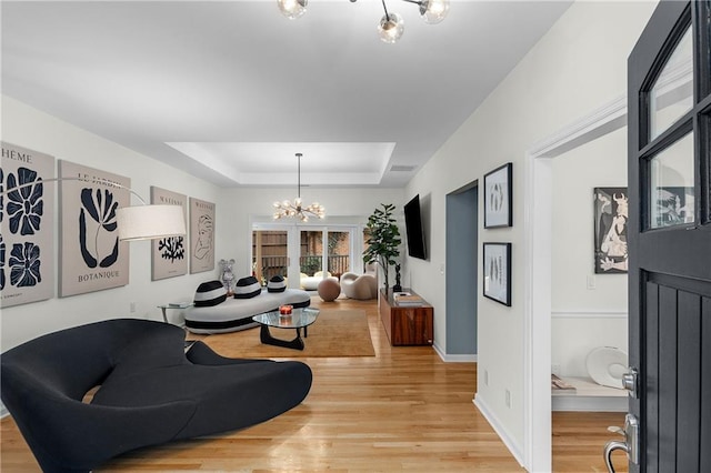 living room with an inviting chandelier, a raised ceiling, and hardwood / wood-style floors