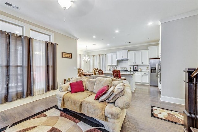 living room featuring ceiling fan with notable chandelier, light hardwood / wood-style flooring, and ornamental molding