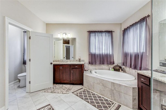 bathroom with tiled tub, vanity, toilet, and tile patterned flooring