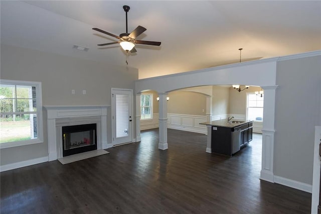 unfurnished living room featuring sink, ceiling fan with notable chandelier, a wealth of natural light, and ornate columns