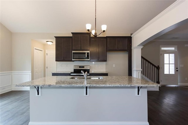 kitchen featuring light stone counters, decorative light fixtures, stainless steel appliances, and a center island with sink