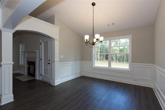 unfurnished dining area featuring a notable chandelier, lofted ceiling, dark hardwood / wood-style floors, and ornate columns