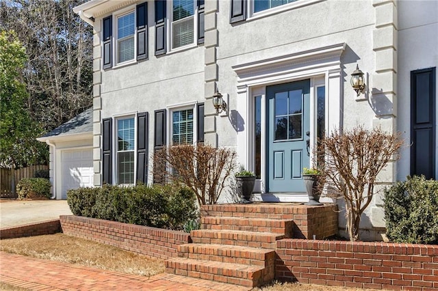 view of exterior entry featuring driveway, an attached garage, and stucco siding