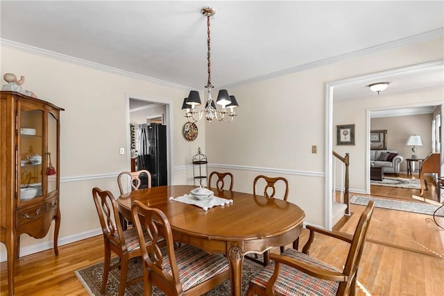 dining area with light wood-style floors, baseboards, ornamental molding, and an inviting chandelier