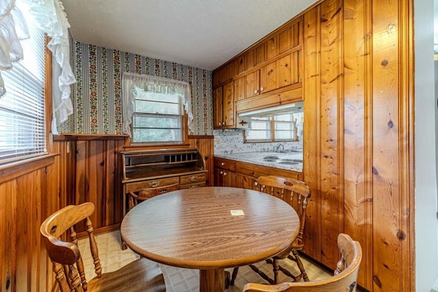 kitchen featuring wood walls, light countertops, wainscoting, brown cabinets, and wallpapered walls