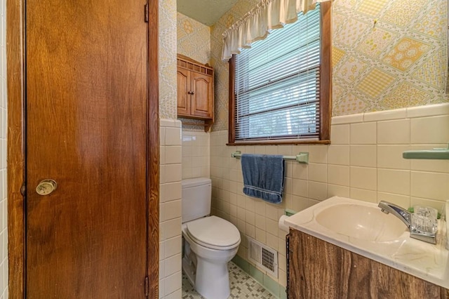 bathroom featuring toilet, a wainscoted wall, vanity, visible vents, and wallpapered walls