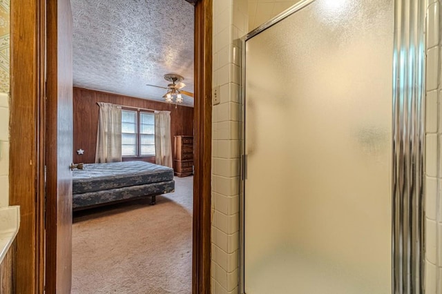 ensuite bathroom featuring a stall shower, wooden walls, a ceiling fan, ensuite bathroom, and a textured ceiling