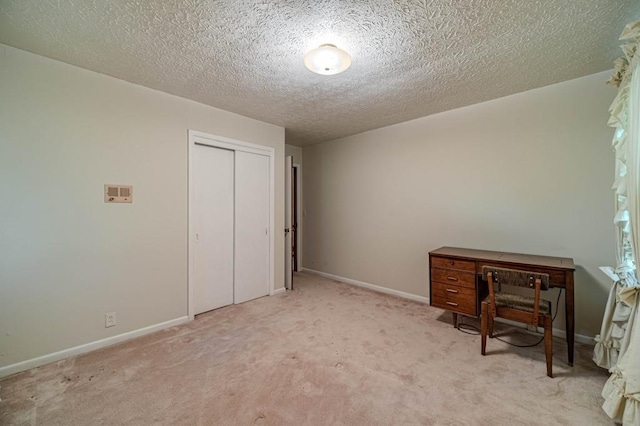 unfurnished bedroom featuring a textured ceiling, baseboards, a closet, and light colored carpet