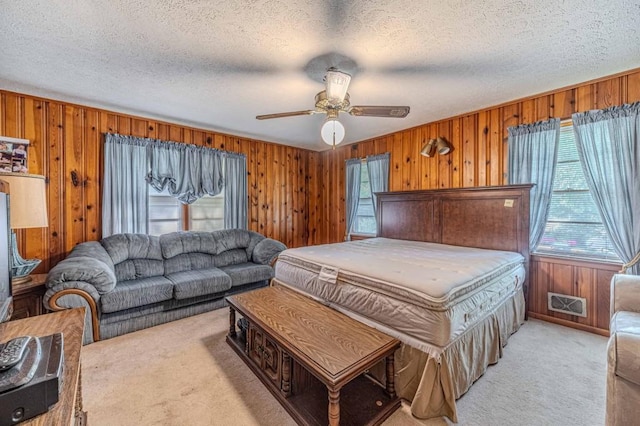 bedroom featuring light carpet, wood walls, a textured ceiling, and ceiling fan