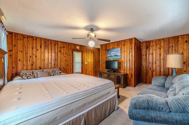 bedroom featuring a ceiling fan, light colored carpet, a textured ceiling, and wooden walls