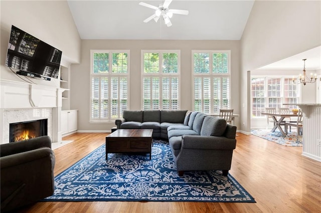 living area with a premium fireplace, baseboards, wood finished floors, and ceiling fan with notable chandelier