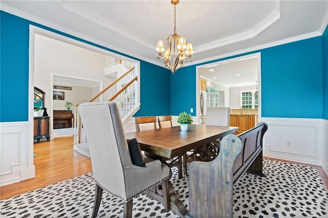 dining room featuring a chandelier, a raised ceiling, a wainscoted wall, and wood finished floors