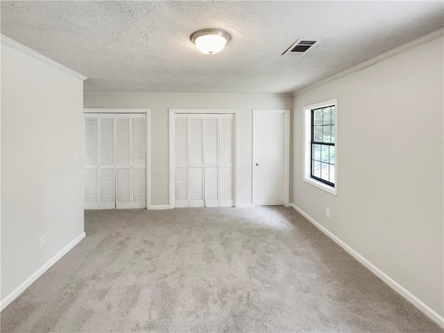 unfurnished bedroom featuring a textured ceiling, light colored carpet, crown molding, and multiple closets