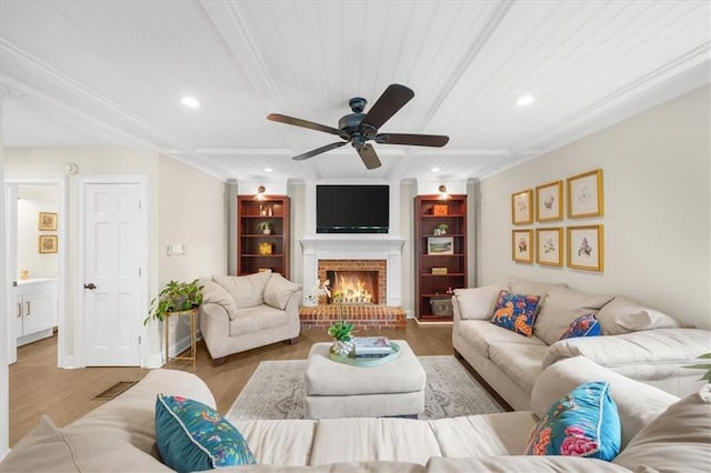 living room with a brick fireplace, hardwood / wood-style flooring, built in features, and ceiling fan